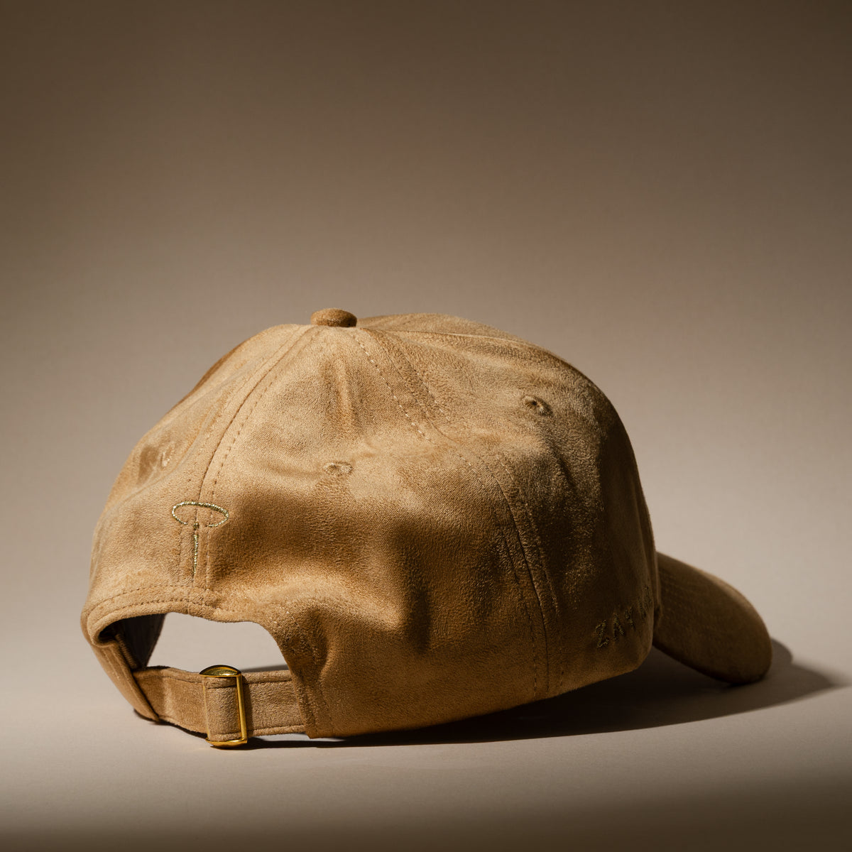 Rear three-quarter view of the ZAY AURA DUNE sand-colored baseball cap with suede texture, embroidered halo logo and adjustable strap with gold-tone buckle.